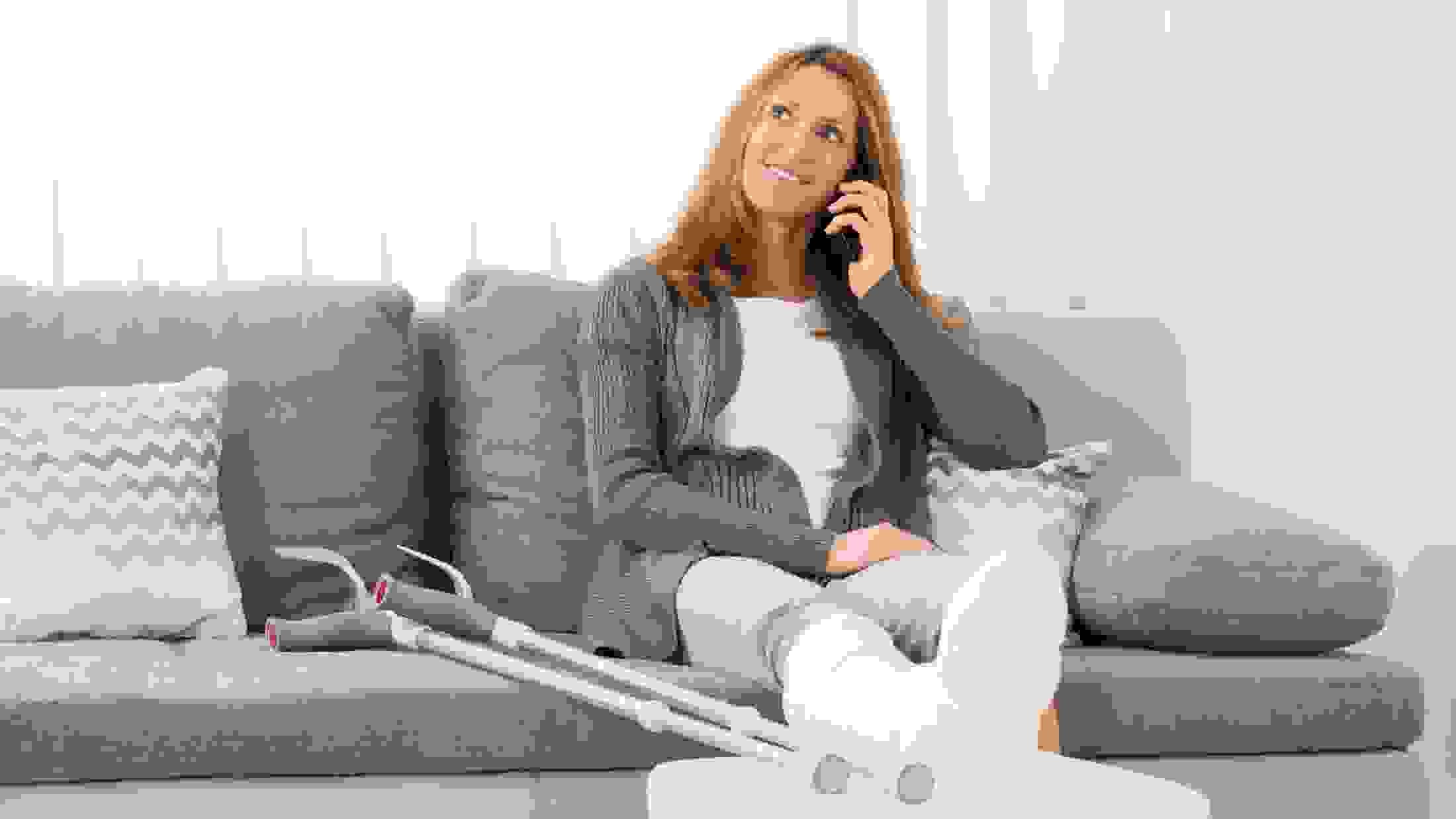 Woman with plastered leg talking on mobile phone at home