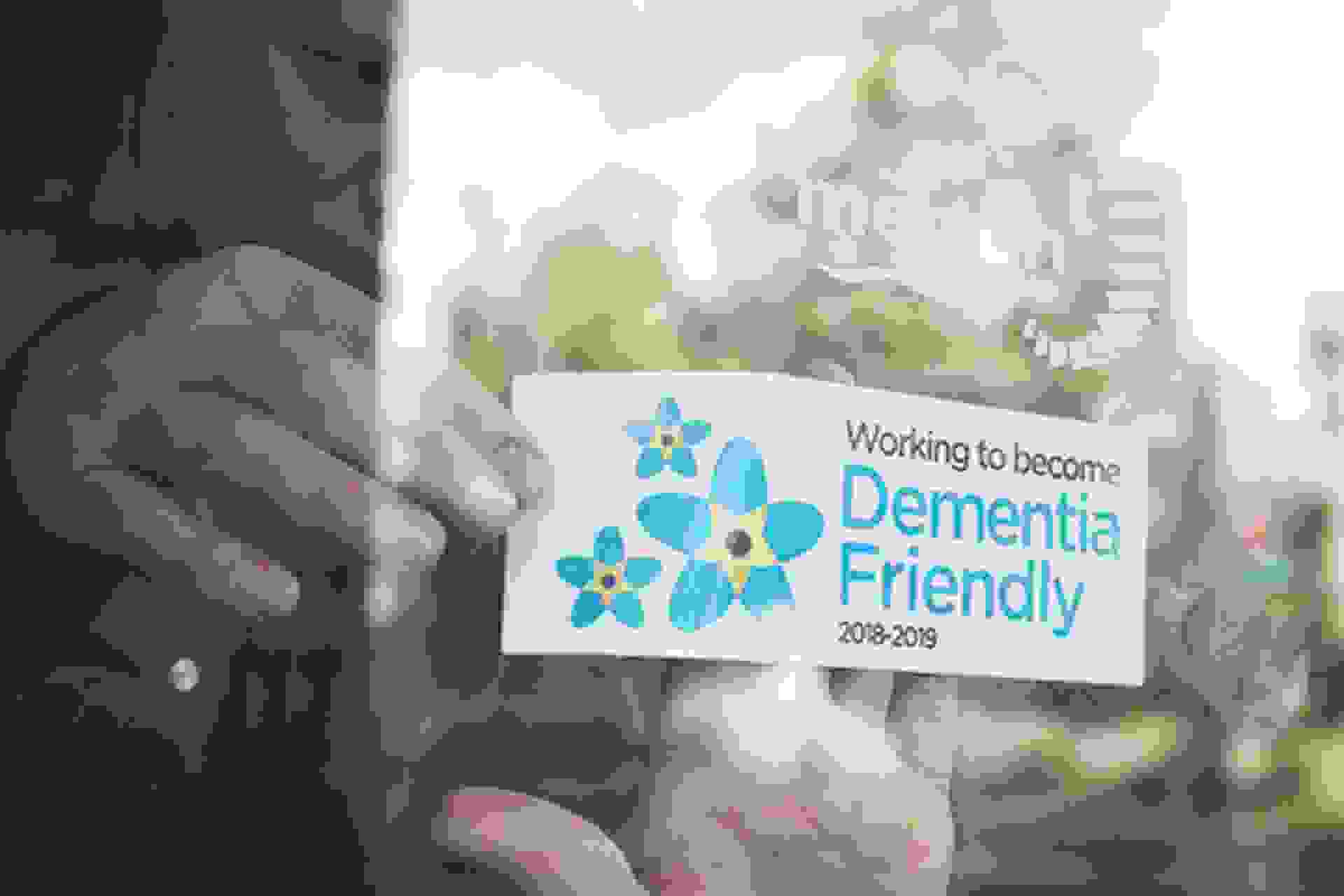A person holding a card that reads, "Working to become dementia friendly 2018 to 2019"