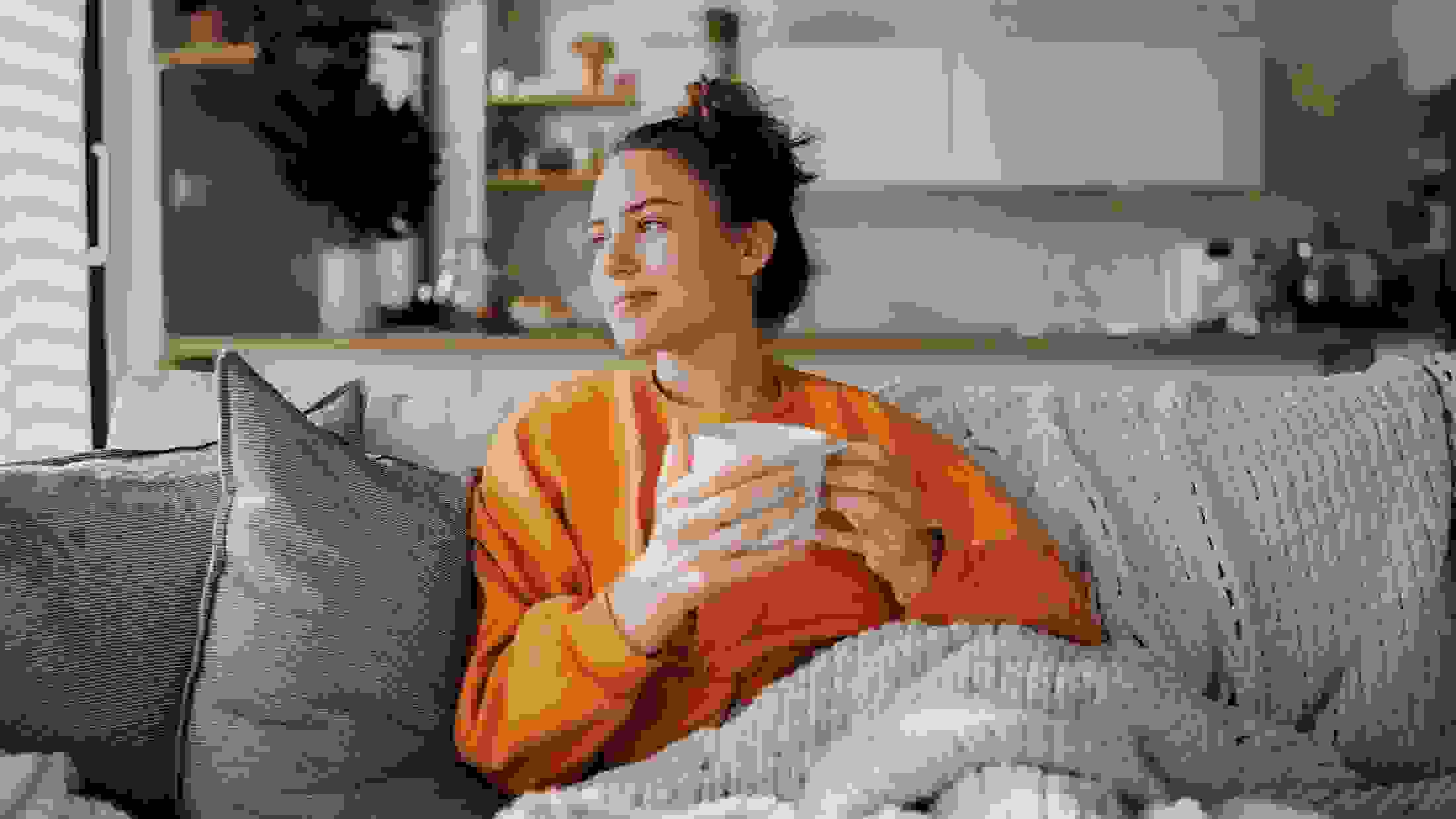 Young woman resting on sofa with blanket and cup of tea