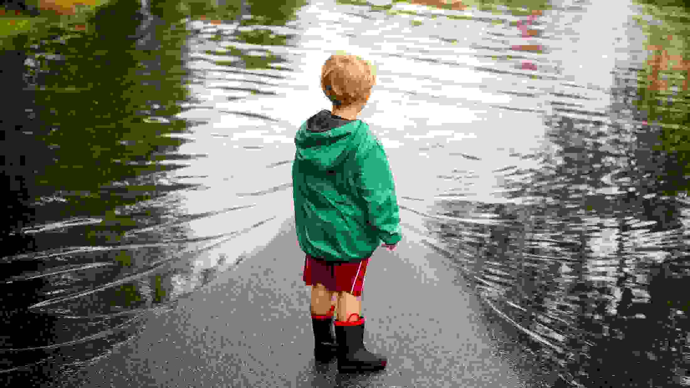 Young boy wearing wellies and an anorak as he stands near flood puddles