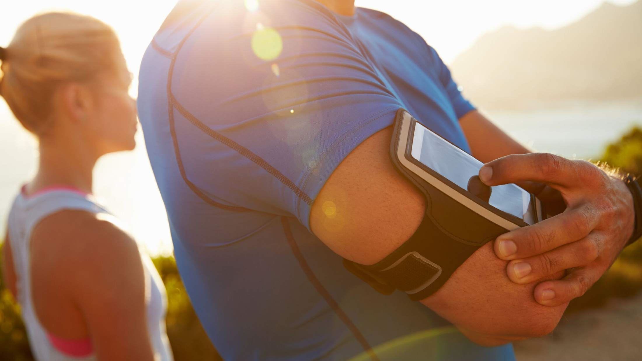Man with smartphone strapped to his arm accompanied by a woman going for a jog