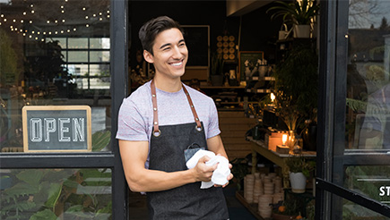 A cafe owner outside of their shop, wearing an apron.