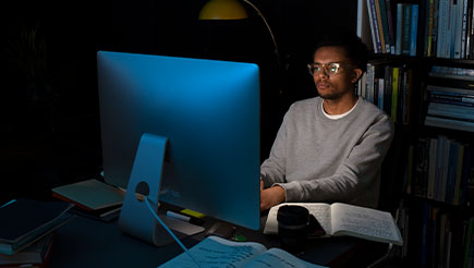 A man looking at his computer screen while sitting in the dark