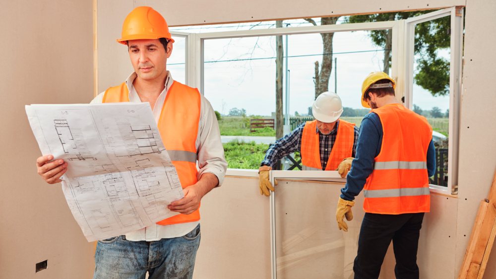 Builder looking at plans while a window is being fitted