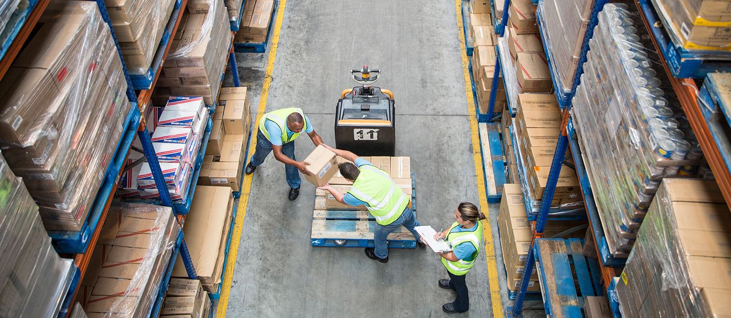 Two people in high vis vests passing boxes in a warehouse as part of a supply chain. 