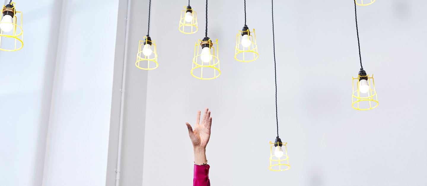 A hand reaching up towards several hanging lightbulbs, trying to grasp one.