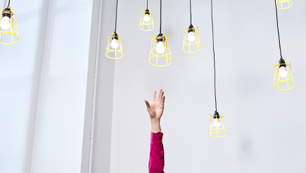 A hand reaching up towards several hanging lightbulbs, trying to grasp one.