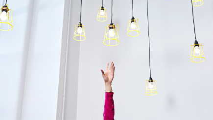 A hand reaching up towards several hanging lightbulbs, trying to grasp one.