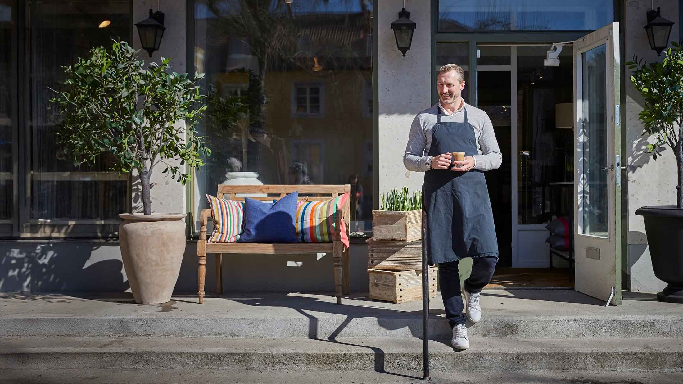 A handsome middle-aged owner holding coffee mug while moving down from steps outside his store