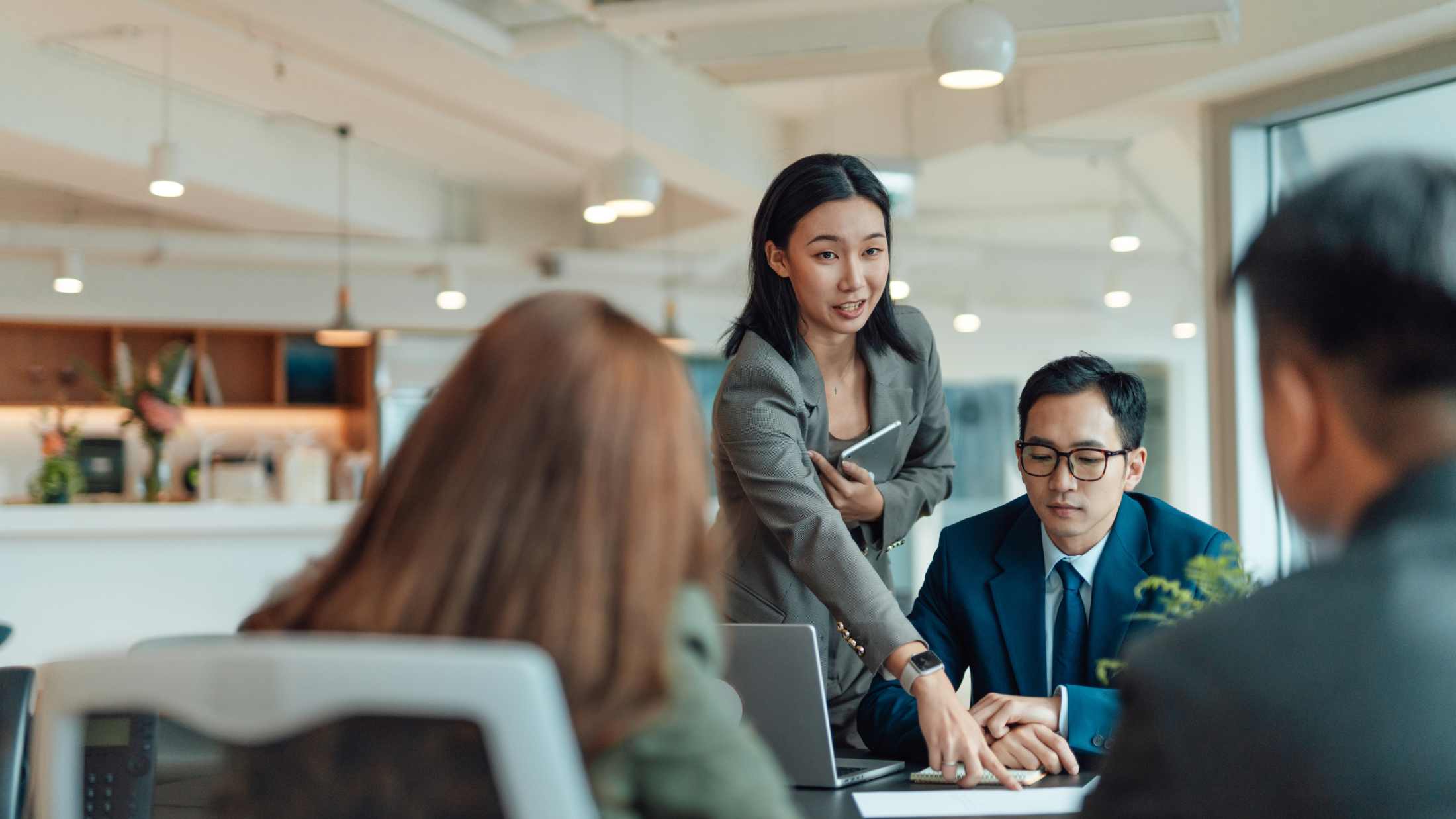 Asian coworkers having a discussion on business strategy, sharing documents with data analysis, sitting at working table in a bright and modern office