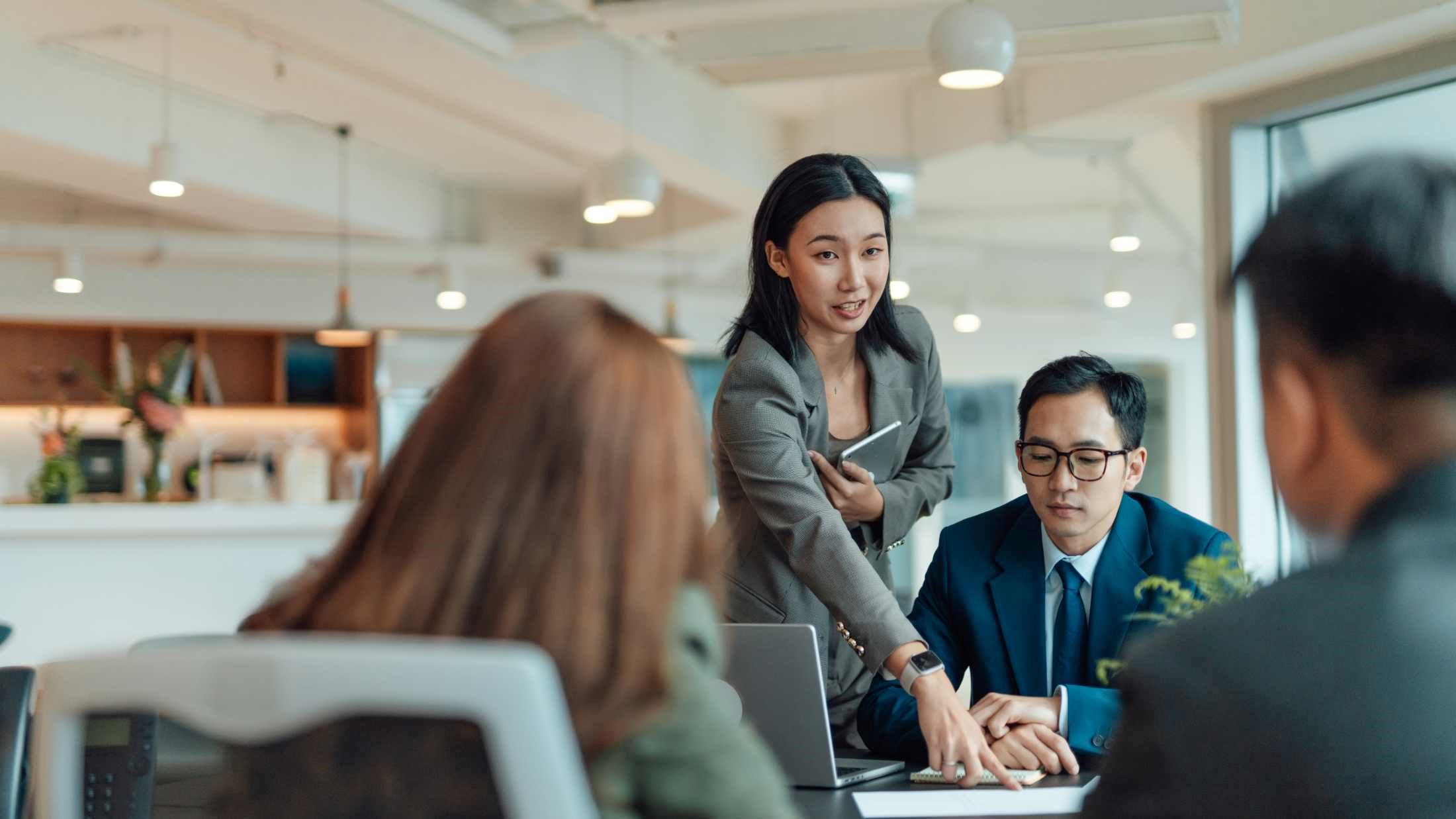 Asian coworkers having a discussion on business strategy, sharing documents with data analysis, sitting at working table in a bright and modern office