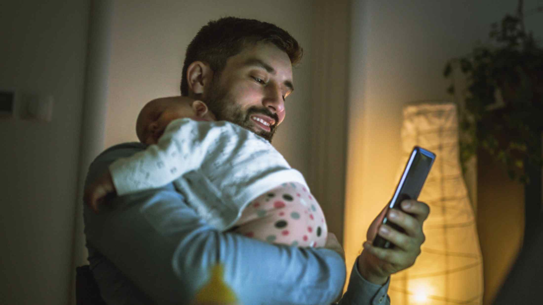 Dad with baby asleep on his shoulder as he checks his phone