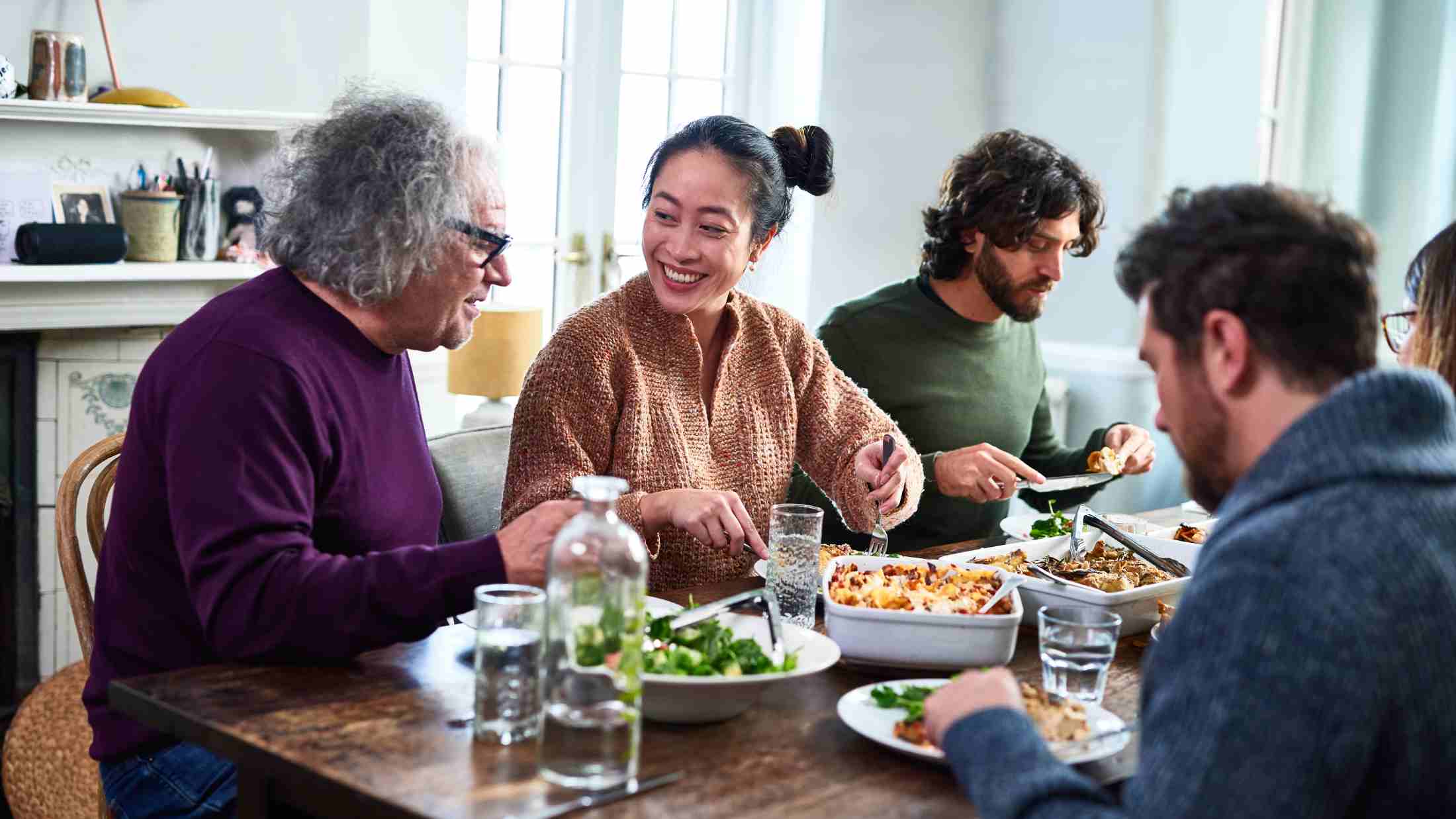Group of mixed aged relatives sitting at dining table enjoying home cooked meal talking and laughing, togetherness, healthy eating, meal time, domestic life