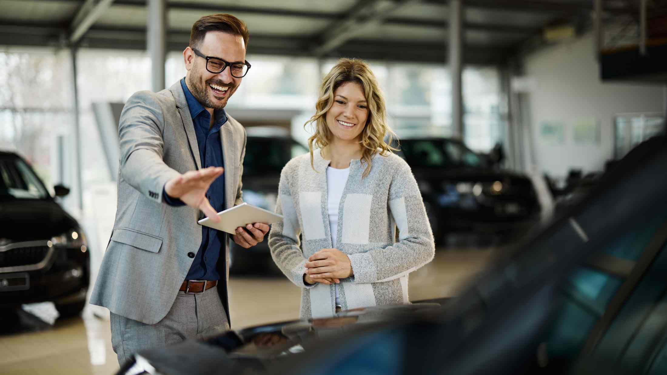 Happy salesman selling the car to his female customer in a showroom