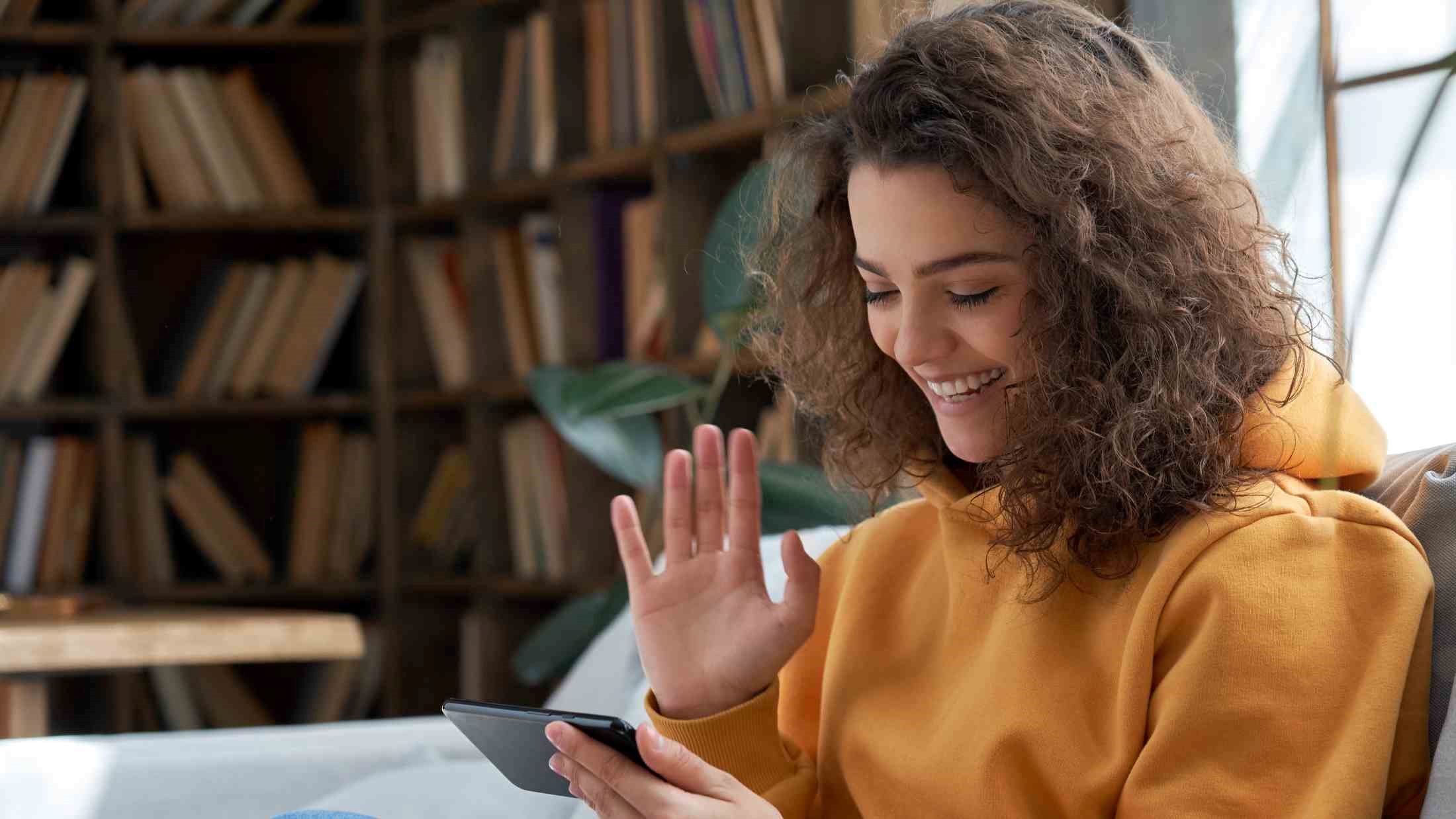 Happy young girl sit on sofa at home holding phone looking at screen