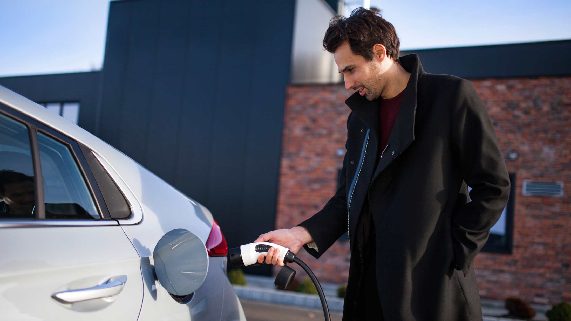 Man on a parking lot, charging a electric car