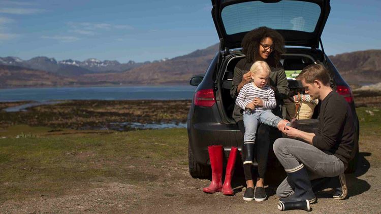 Parents helping son change shoes on car boot