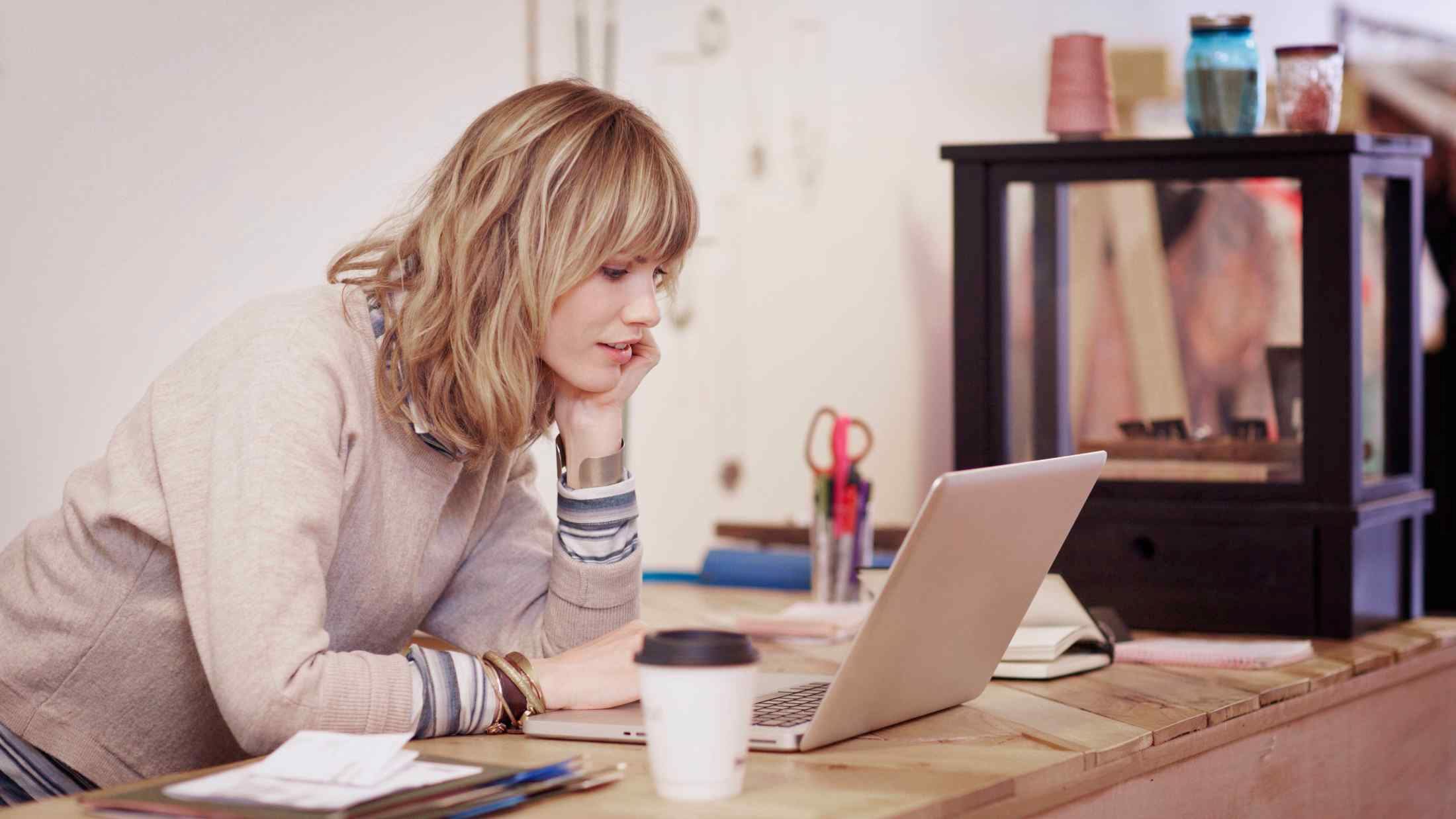 Shop assistant leaning on a store counter and looking at a laptop