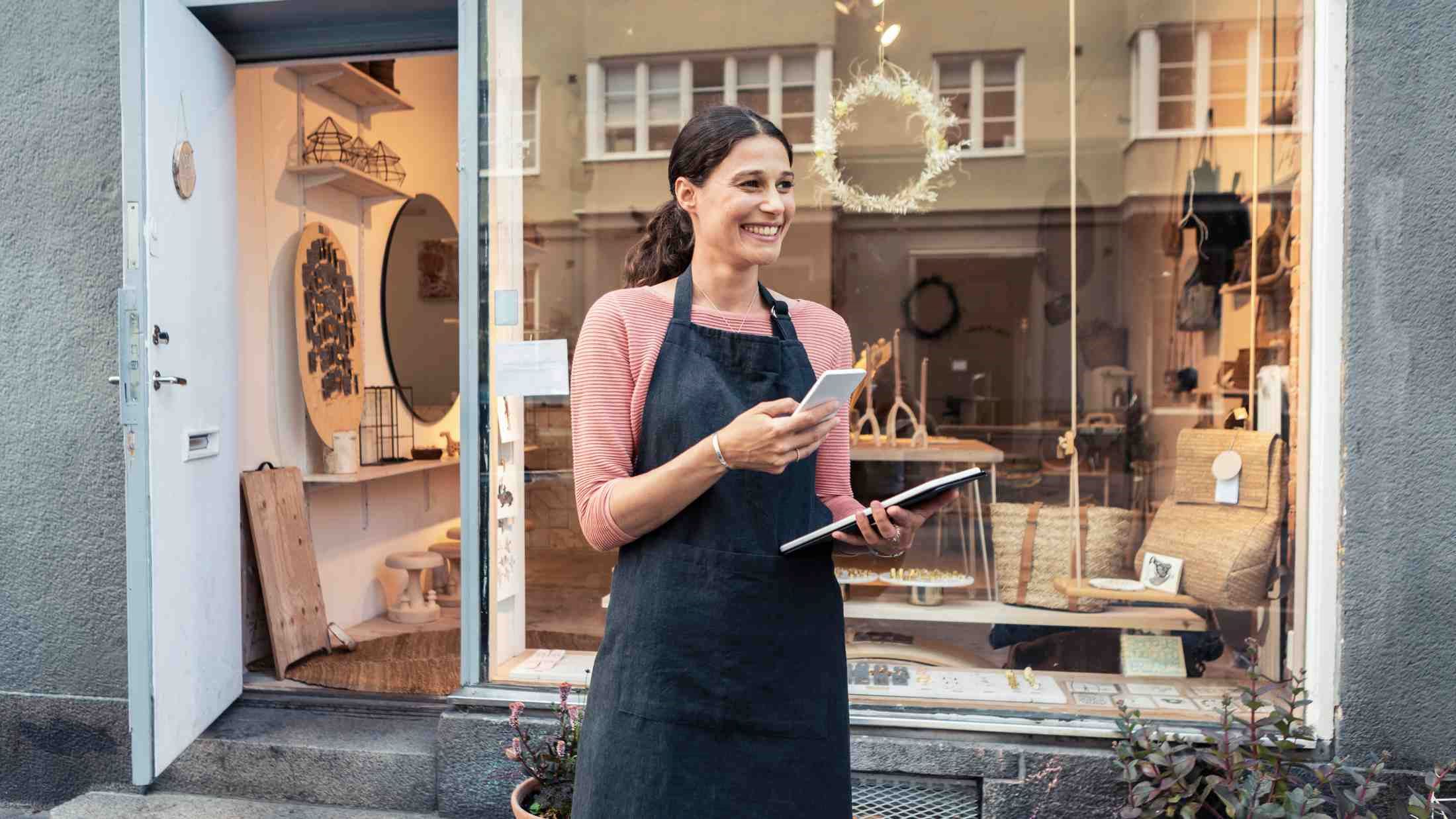 Smiling female entrepreneur with smart phone and digital tablet outside store