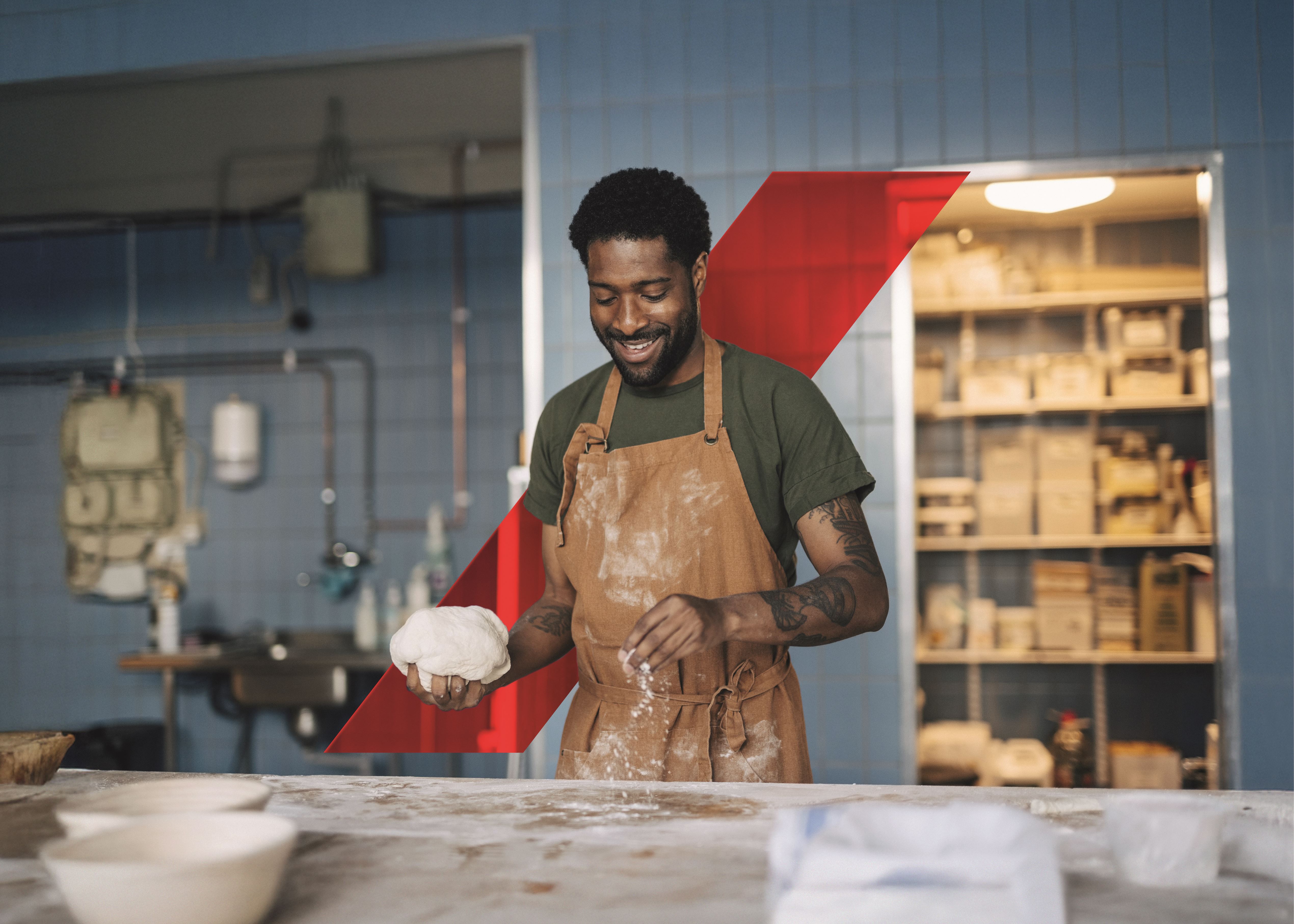 Smiling male baker dusting flour on table and holding dough while working at bakery
