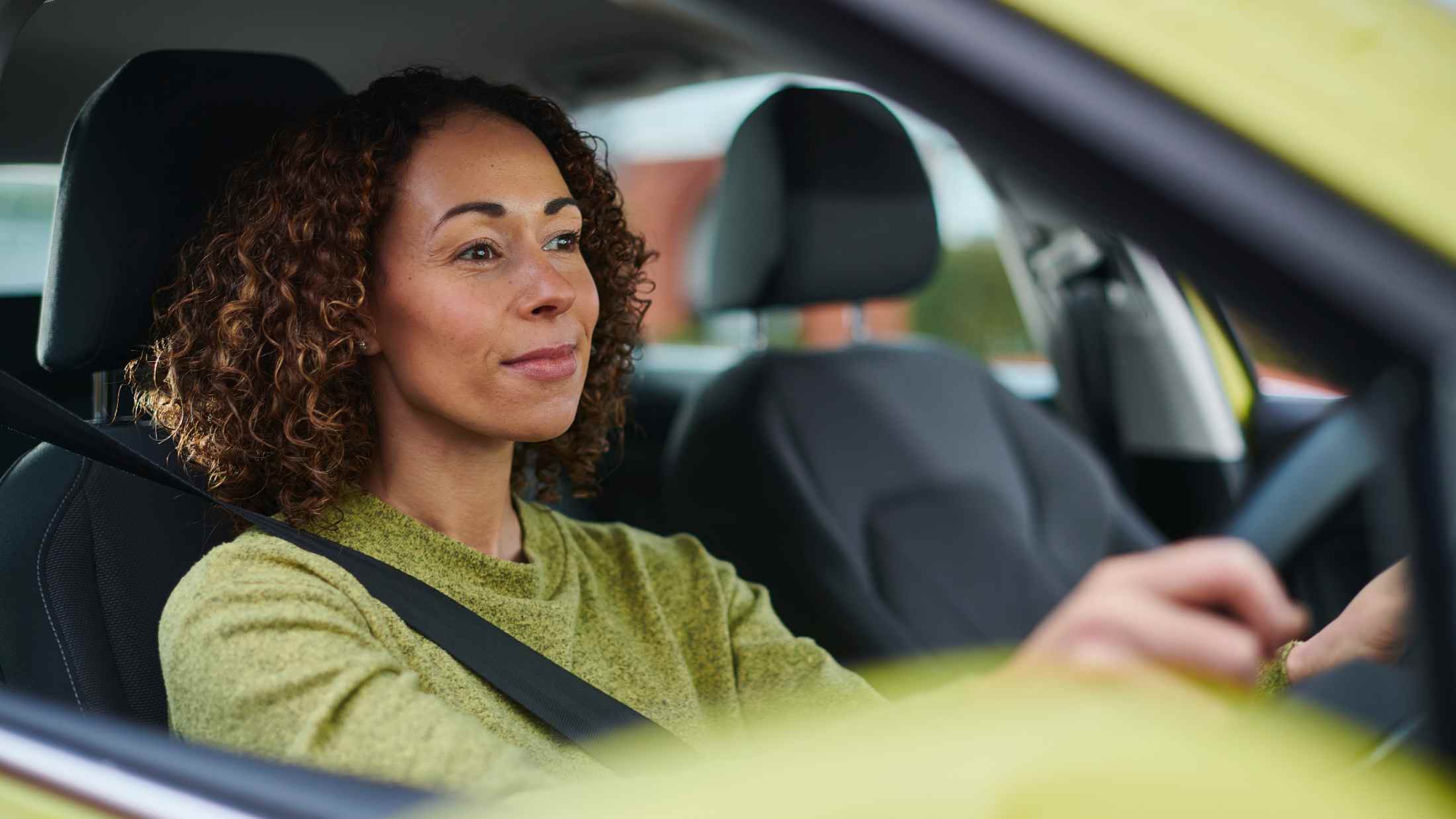 Woman wearing a green jumper drviing a green car