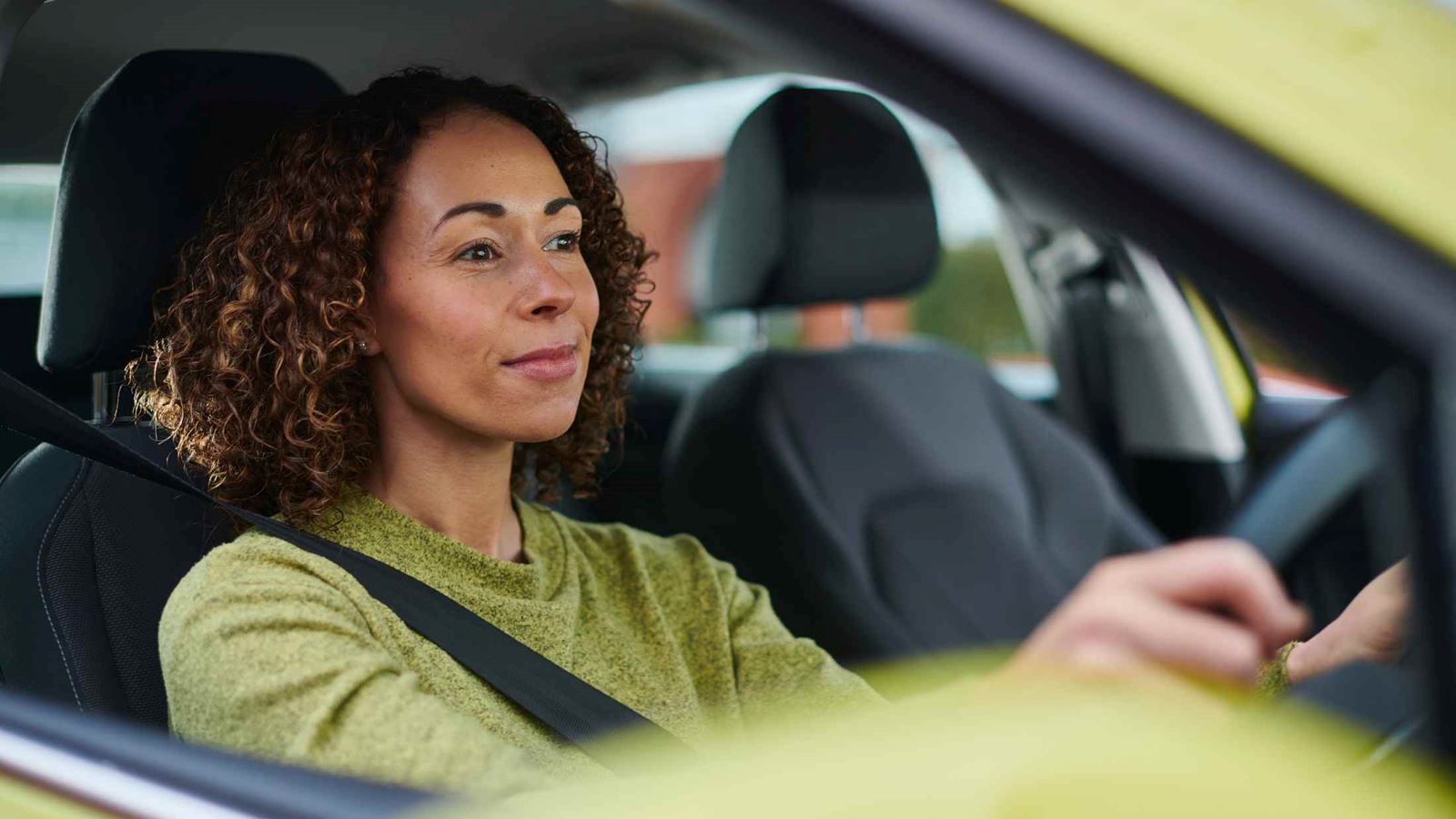 Woman wearing a green jumper drviing a green car