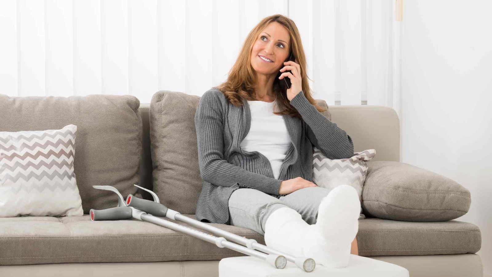 Woman with plastered leg talking on mobile phone at home