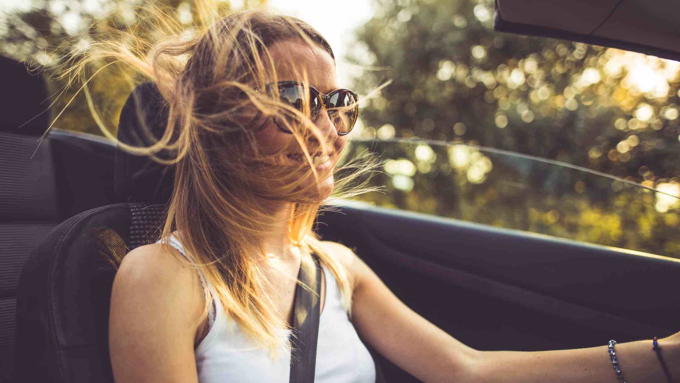 Young woman smiling while driving with the roof down and the wind blows through her hair
