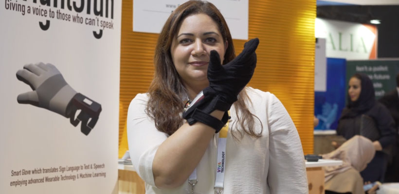 Woman in early 40's with long brown hair at a trade expo wearing the Smart Glove and holding up her hand.