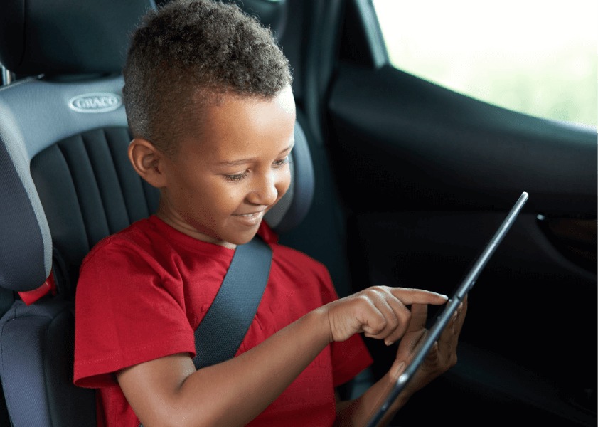 Young child sat in car seat playing on his tablet