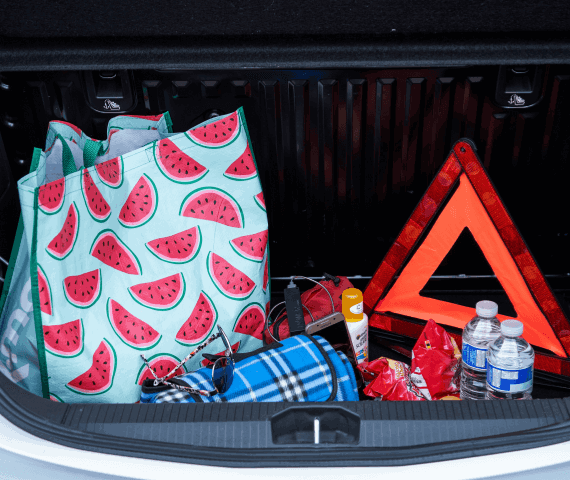 Car boot containing a rug, sunglasses, bottles of water, crisps, water and a warning triangle