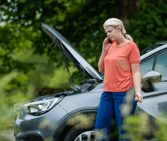 Woman stood by side of road with bonnet up on the phone calling breakdown recovery