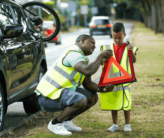 Father and son wearing high-vis jackets stood by side of the road assembling a warning triangle