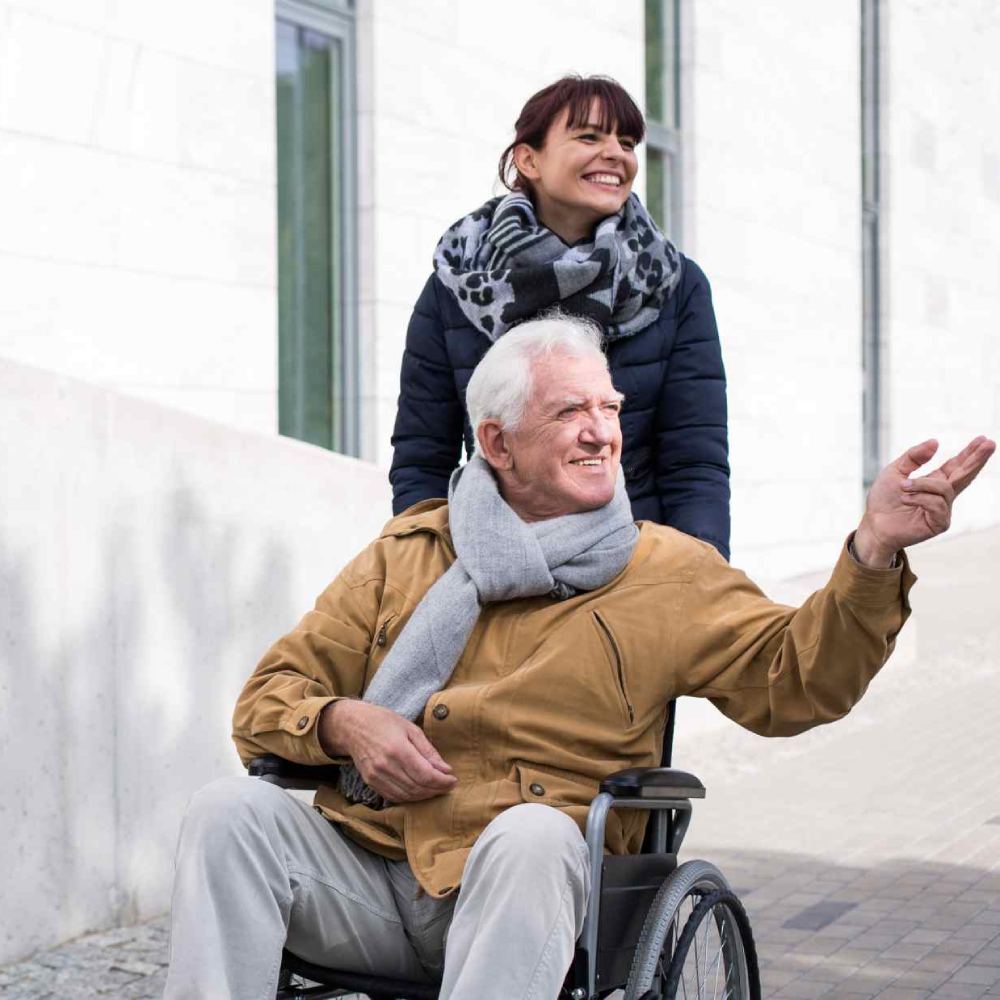 Disabled senior man being pushed in his wheelchair by a woman