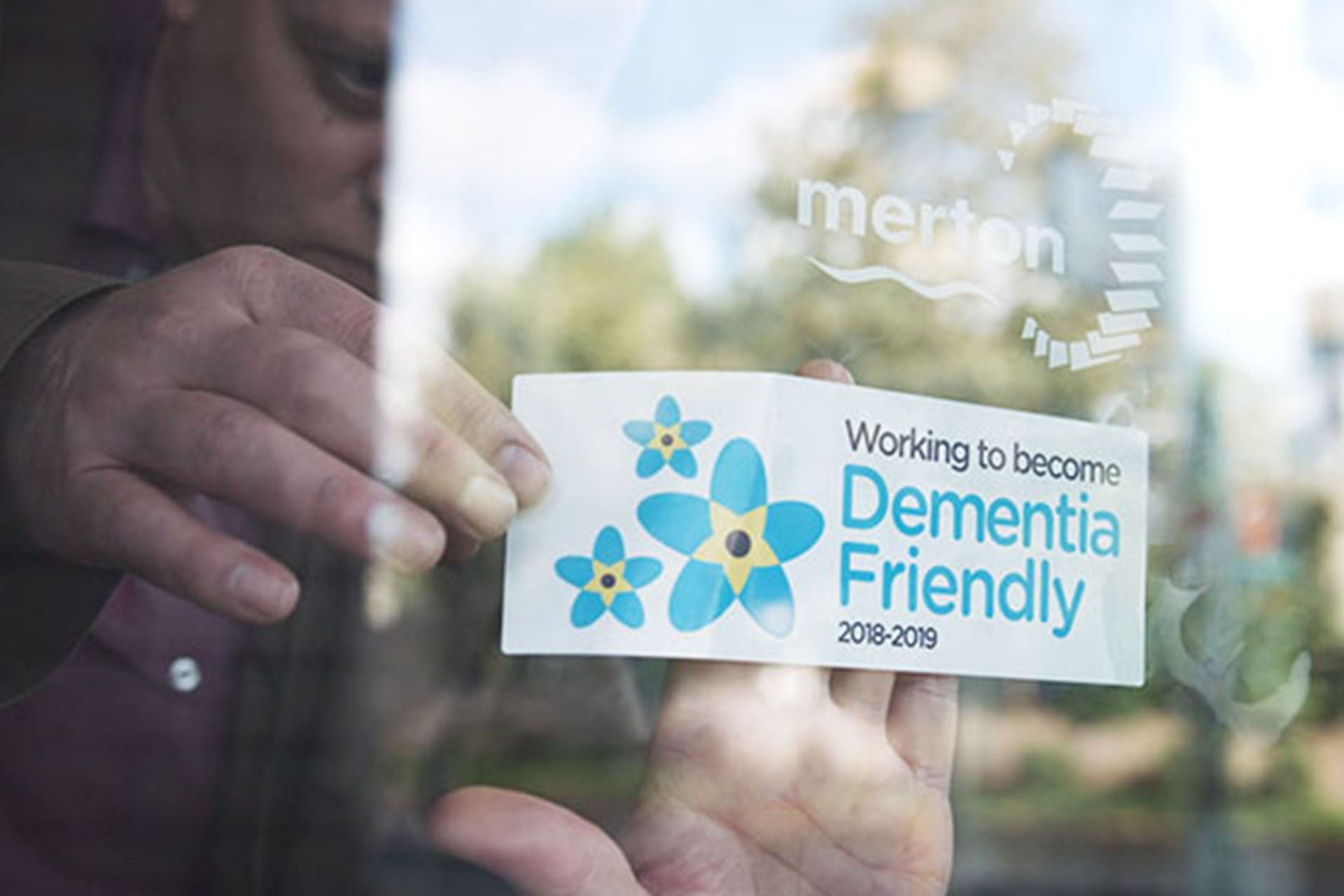 A person holding a card that reads, "Working to become dementia friendly 2018 to 2019"