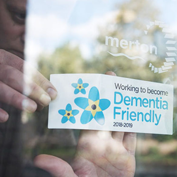 A person holding a card that reads, "Working to become dementia friendly 2018 to 2019