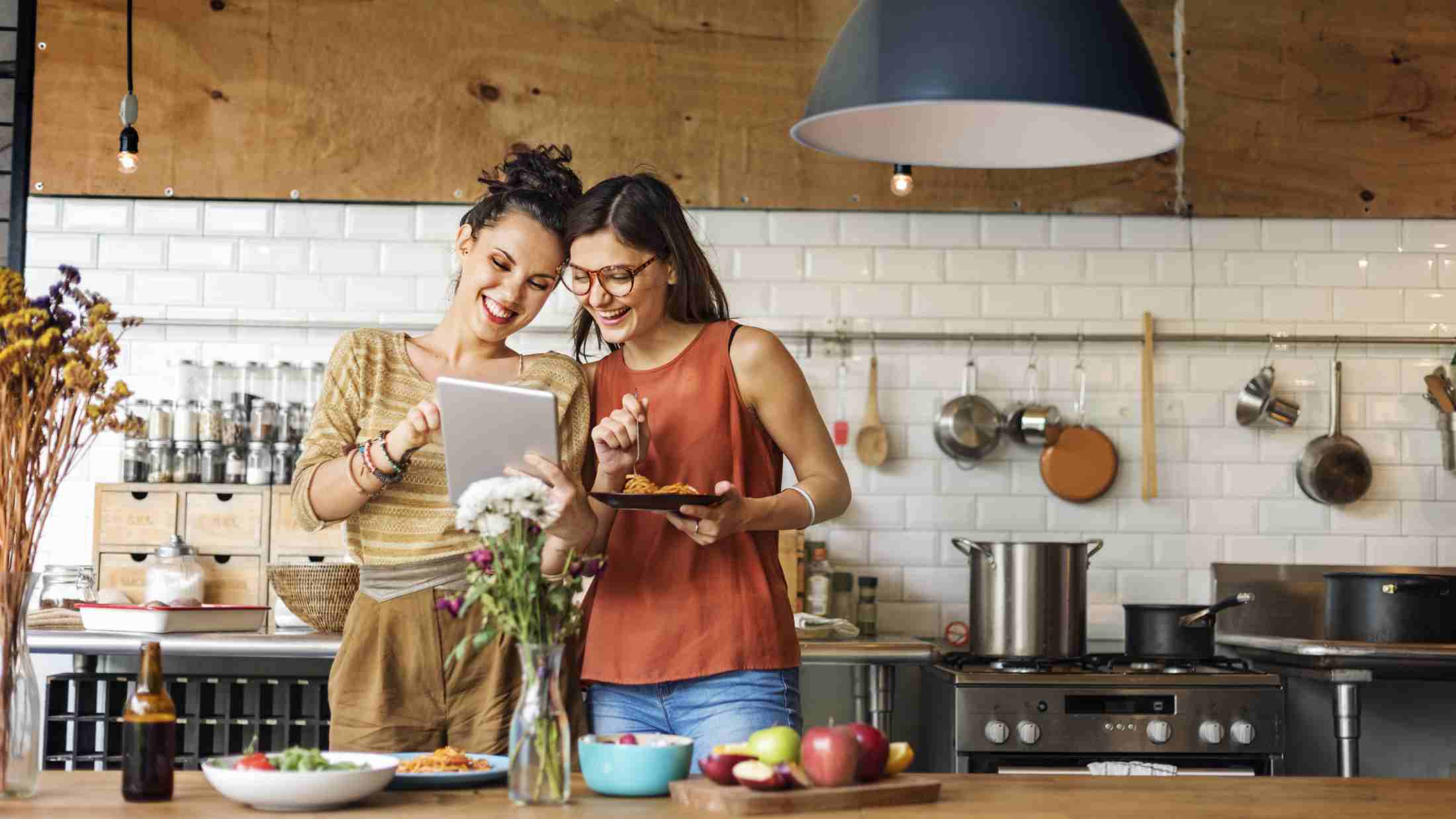Two female friends with a tablet cooking at home