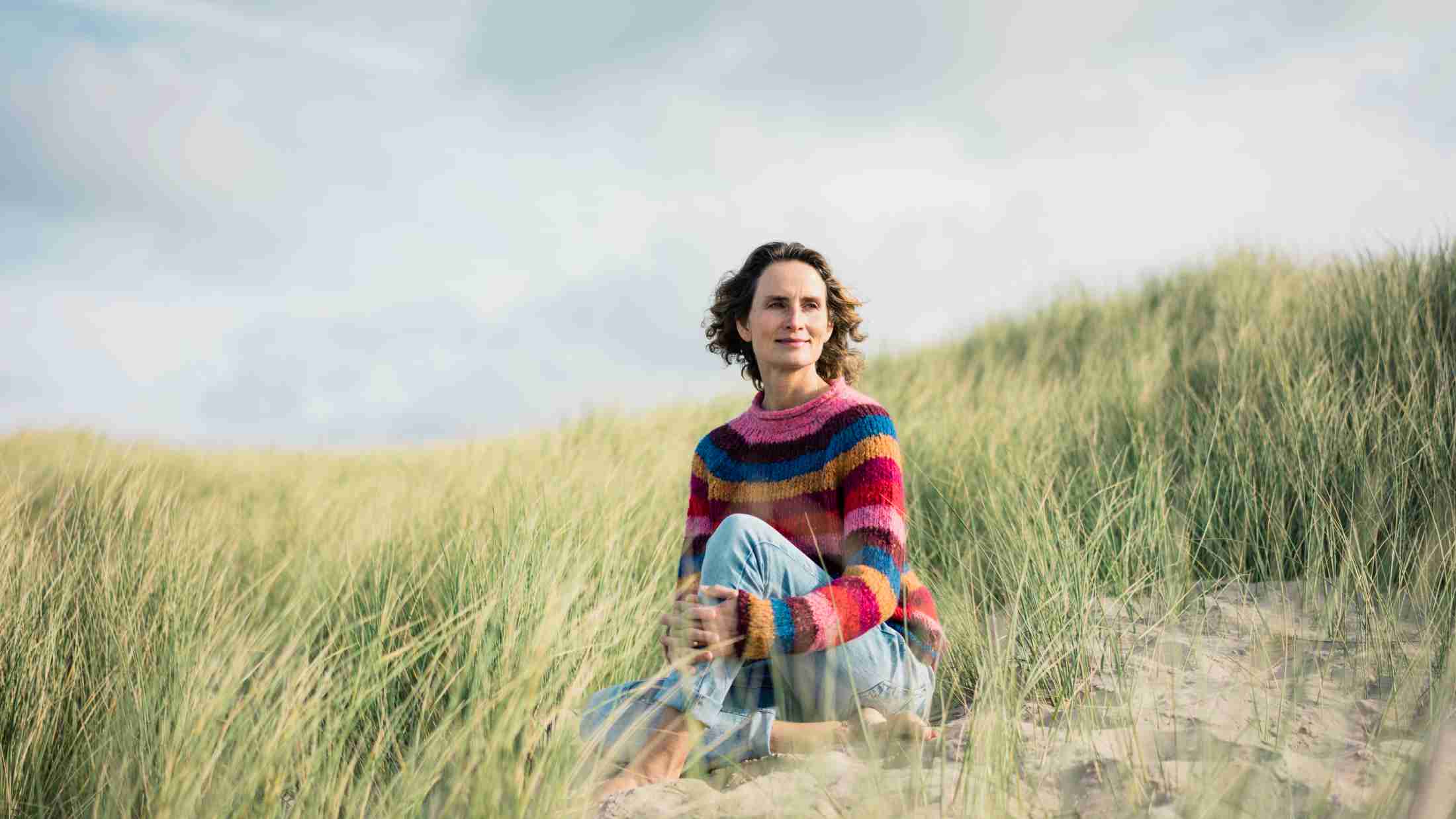 Mature woman relaxing on the beach, sitting in the dunes
