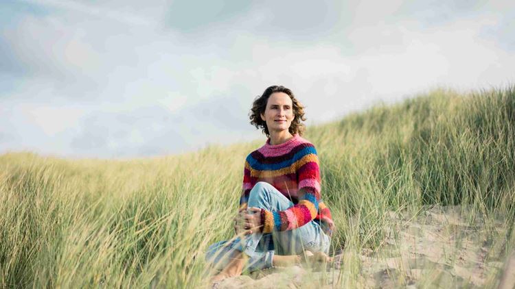 Mature woman relaxing on the beach, sitting in the dunes