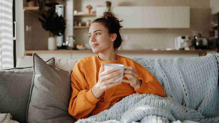 Young woman resting on sofa with blanket and cup of tea