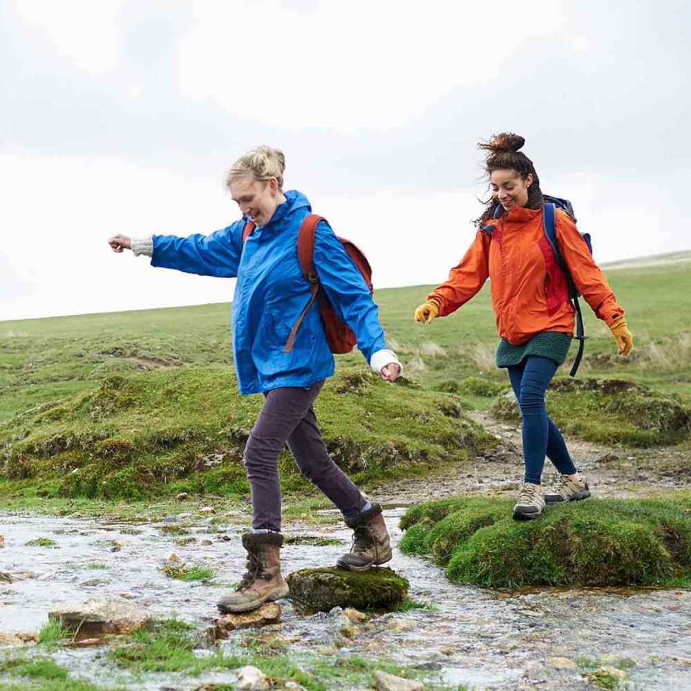 Two hikers crossing stream in countryside