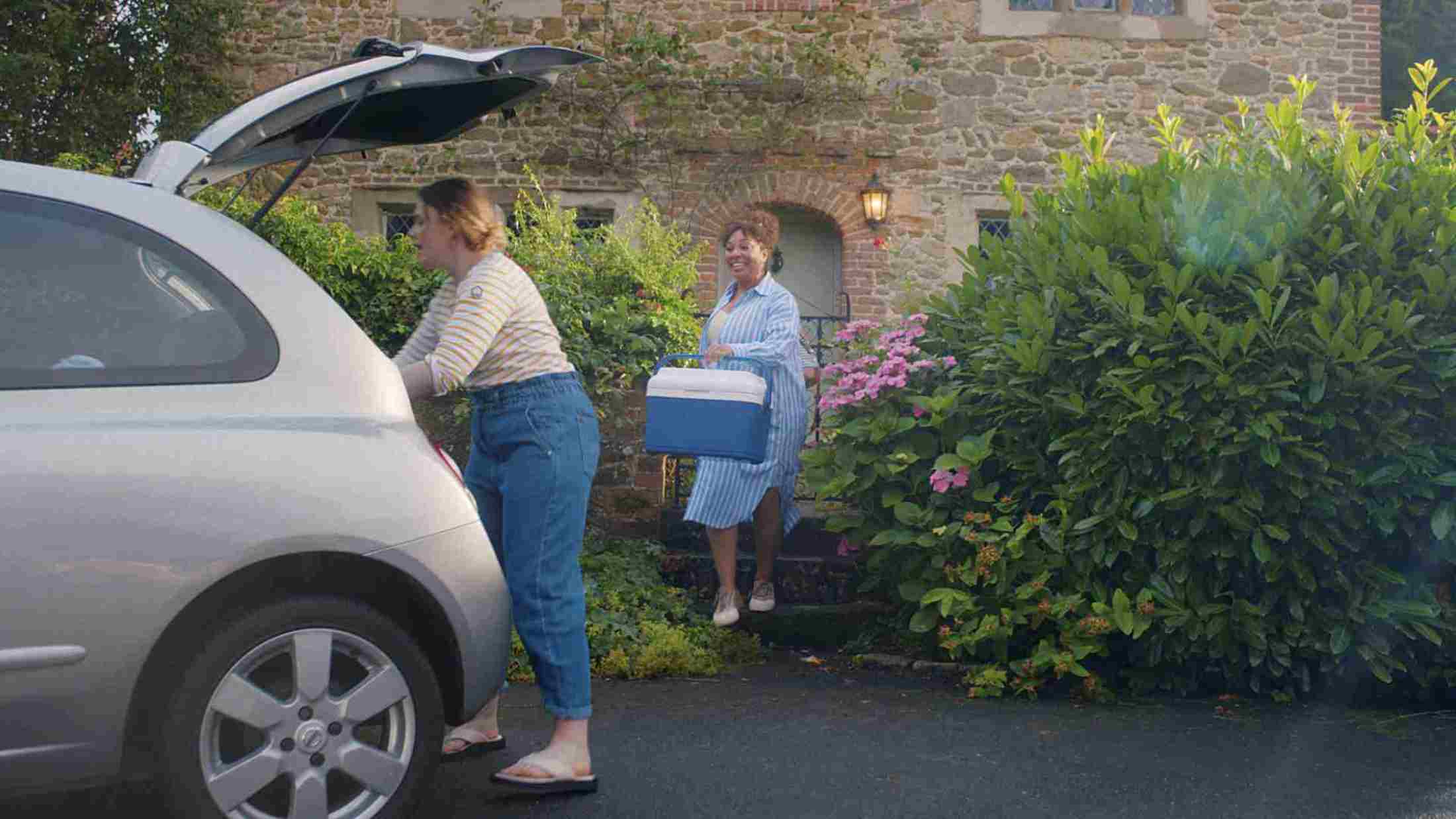 Two women loading a cooler bag in a car boot