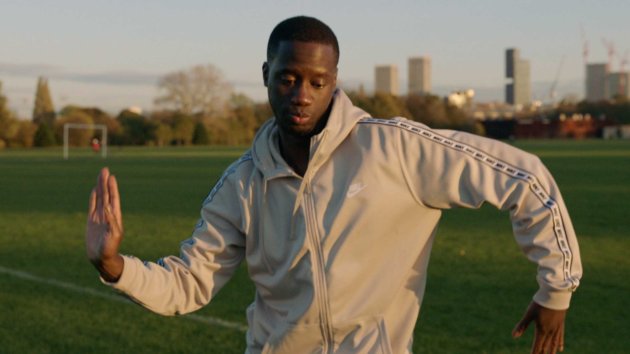 Young black male doing the arm wave dance move while wearing a grey tracksuit top