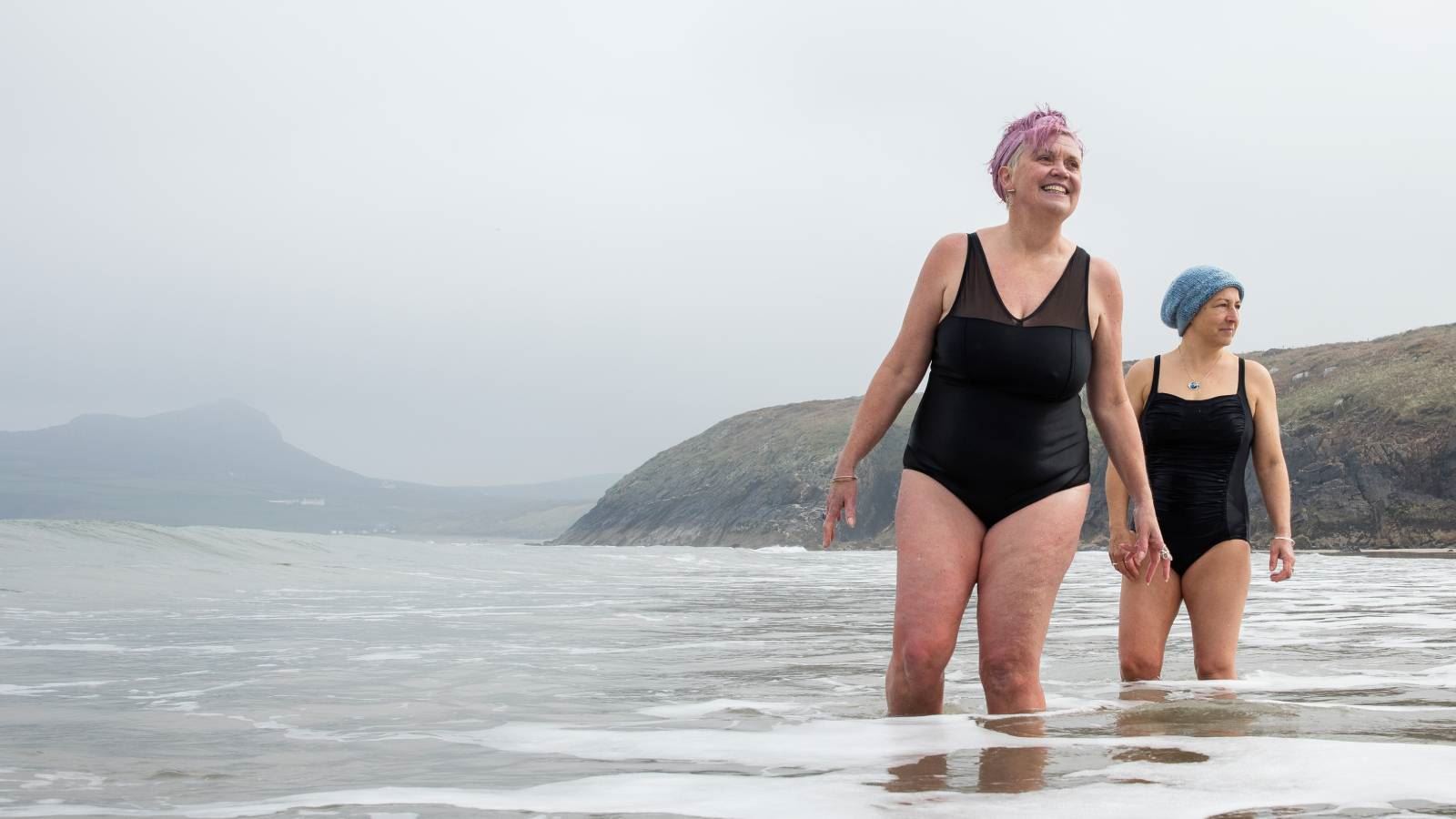 Sam and Sian, from the Bluetits cold water swimmers, standing in the sea in West Wales