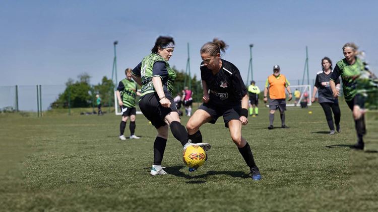 Two women's walking football players compete for the ball