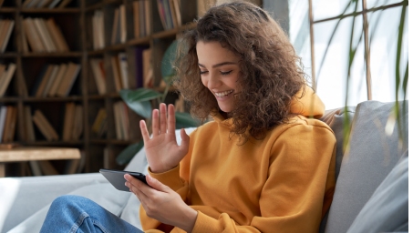 happy young girl sit on sofa at home holding phone looking at screen