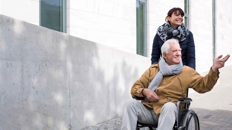 Disabled senior man enjoying a sunny autumn day with his carer