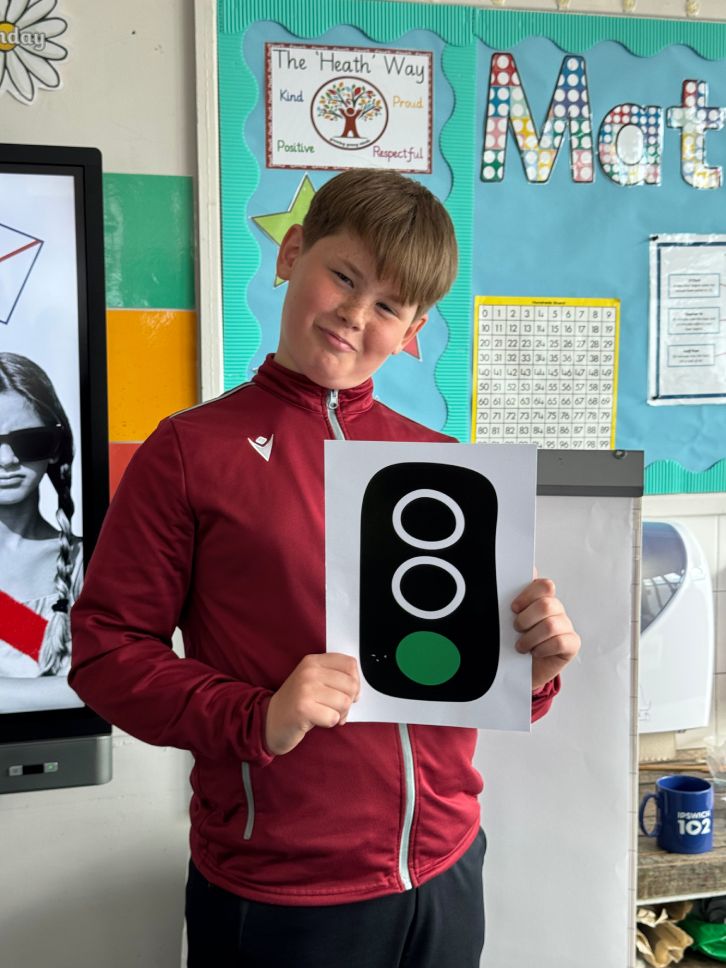 A boy with short brown hair holds a white piece of paper showing a green traffic light.