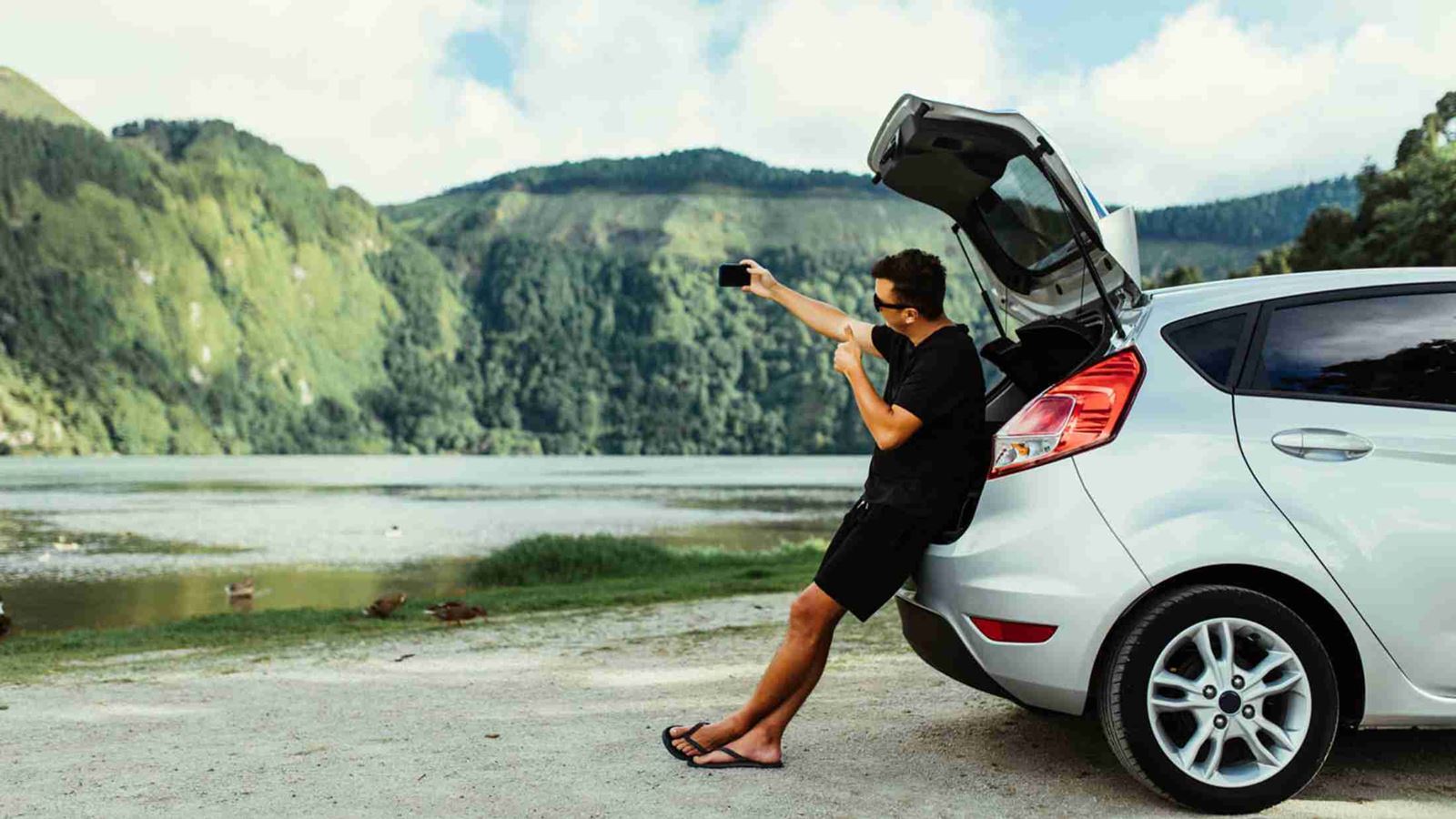 A man taking a selfie at the open hatch back of his car