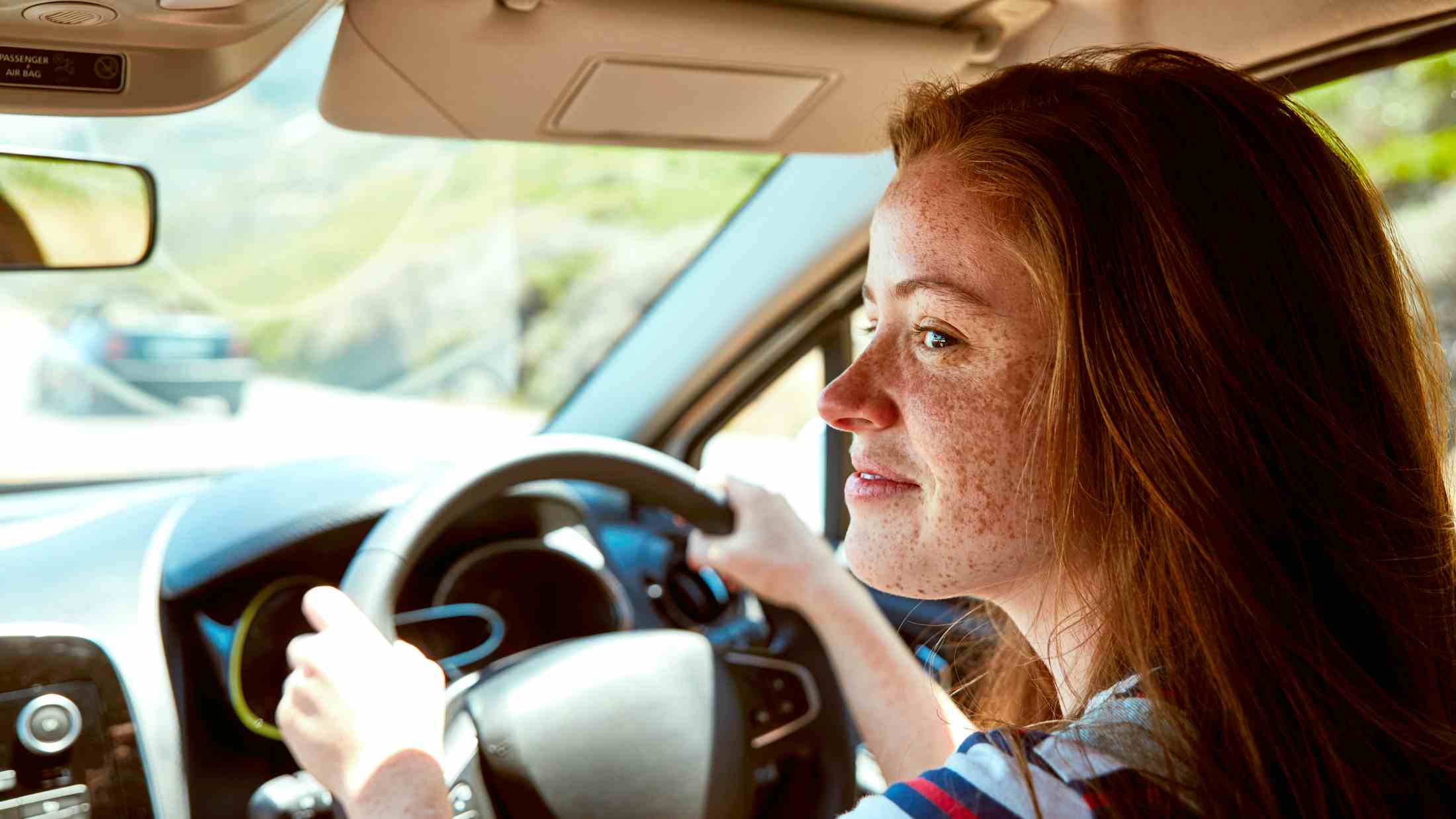 Smiling young woman with freckles driving car looking sideways